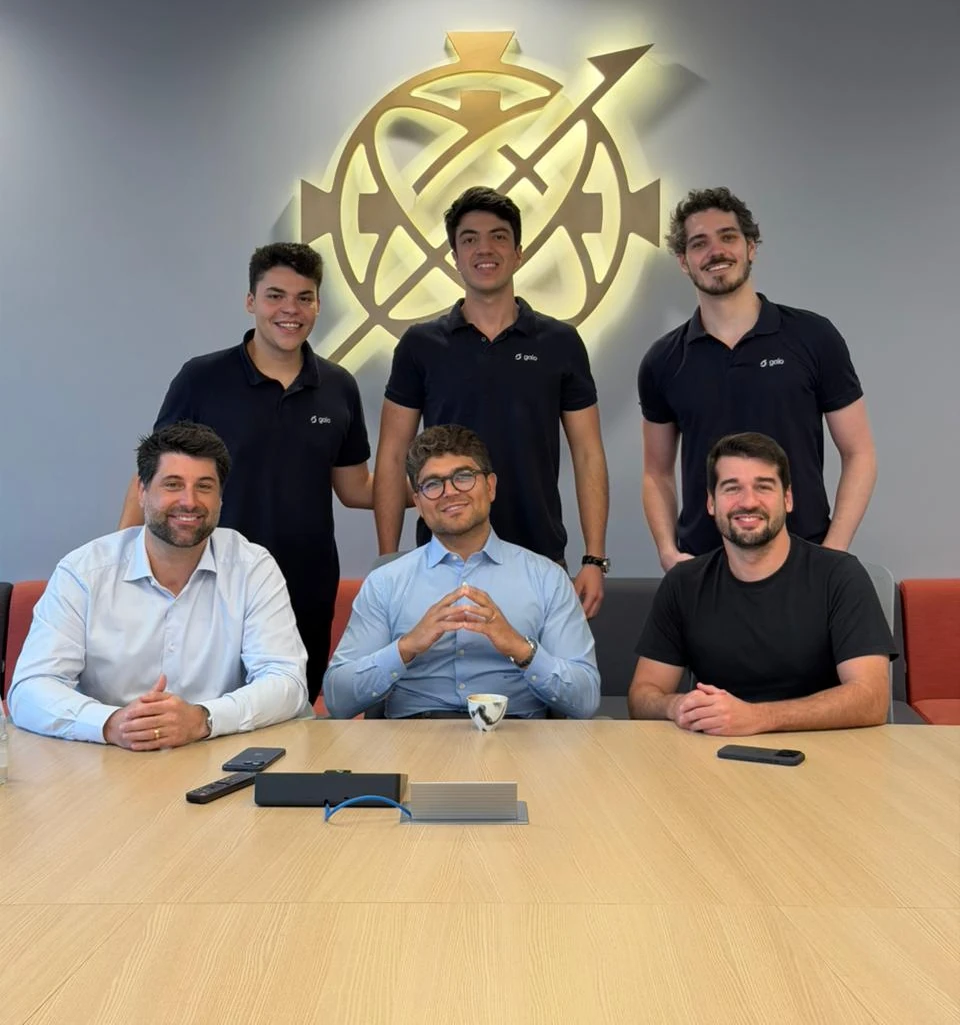 Equipes da Gaio e do G4 reunidas em torno de uma mesa, sob o logo do G4 na parede